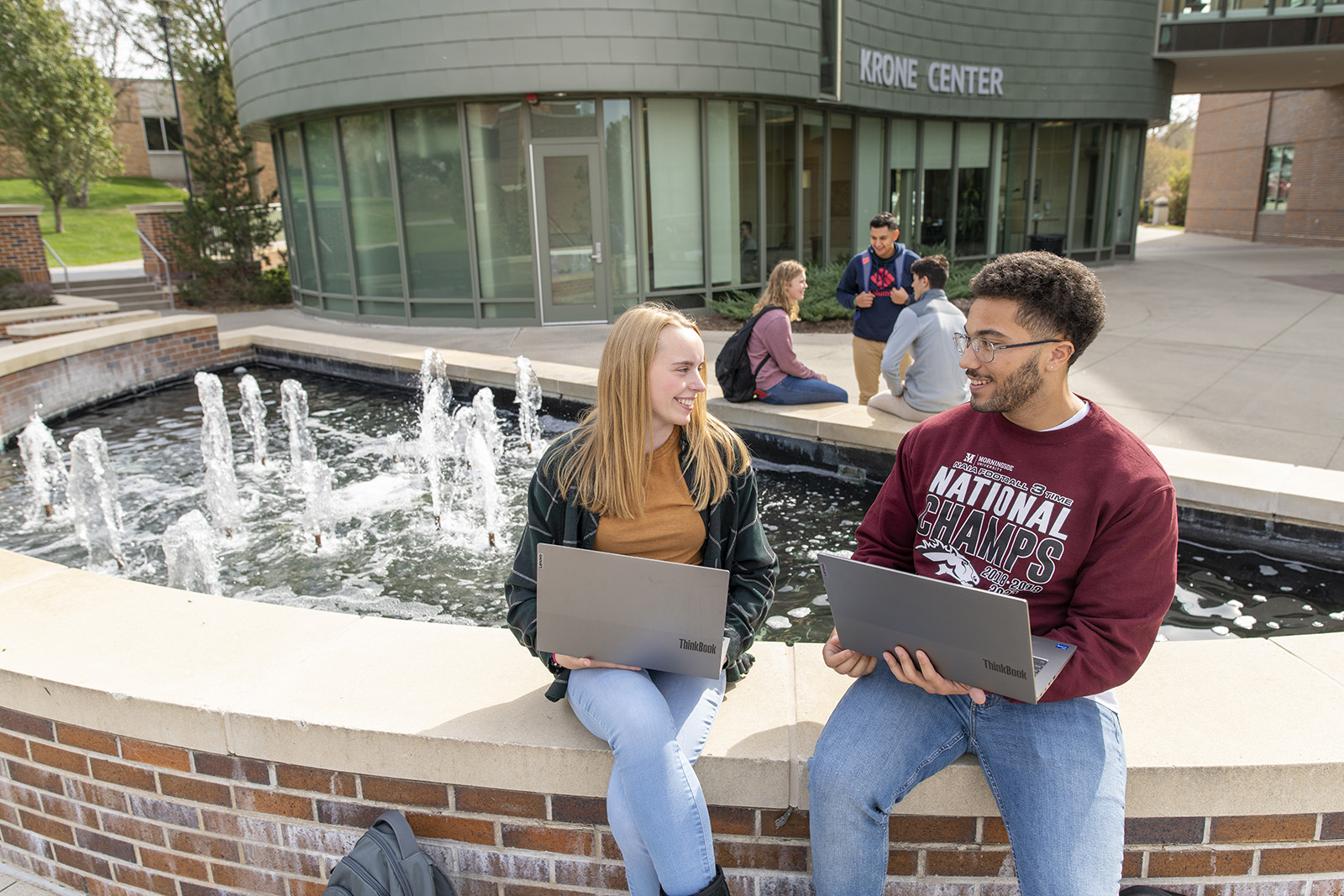 Students sitting with laptops by a fountain