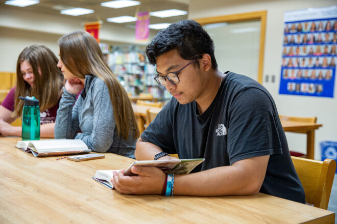 A student sits at a table reading a book