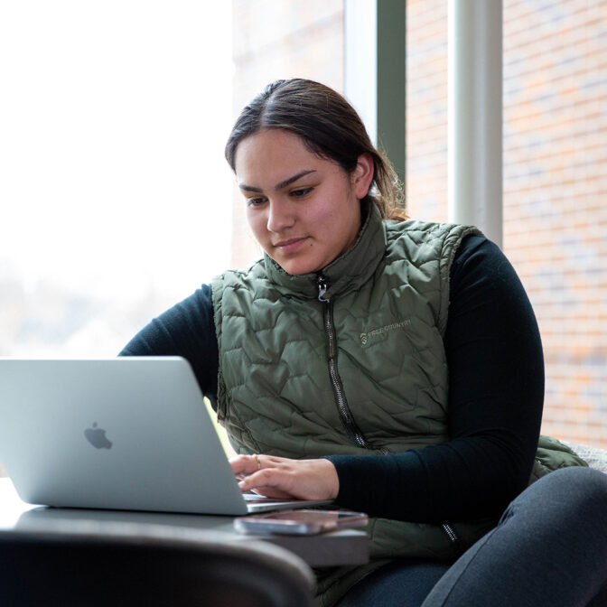 Student working on laptop by a large window