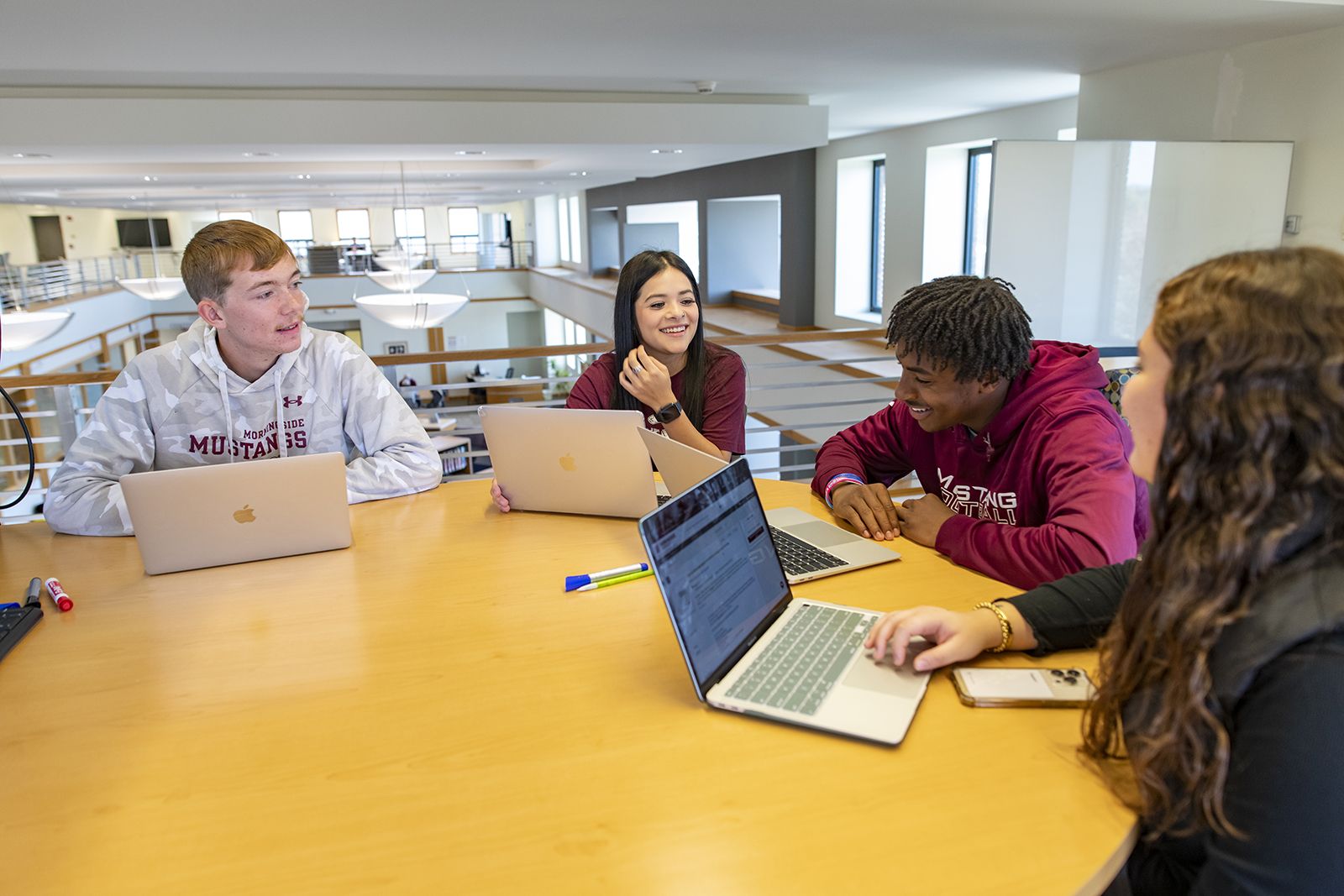 Four students seated at a round table with laptops