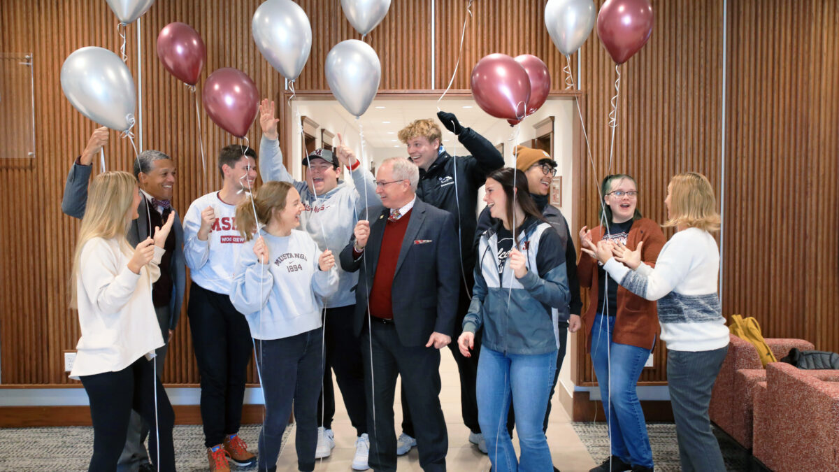 group of around a dozen people holding balloons and celebrating