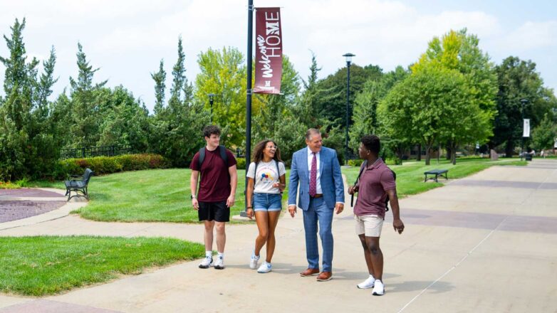 Interim President Chad Benson walks with 3 students on the campus mall