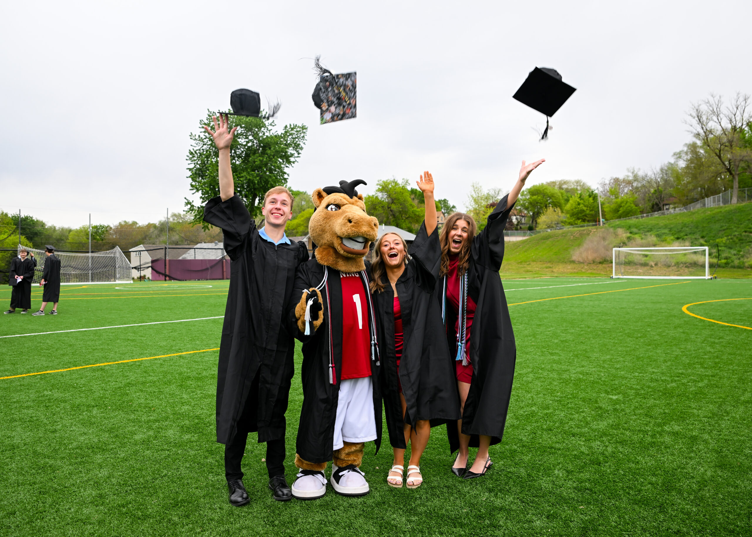 3 students with Monte the Mustang throwing their graduation caps in celebration.