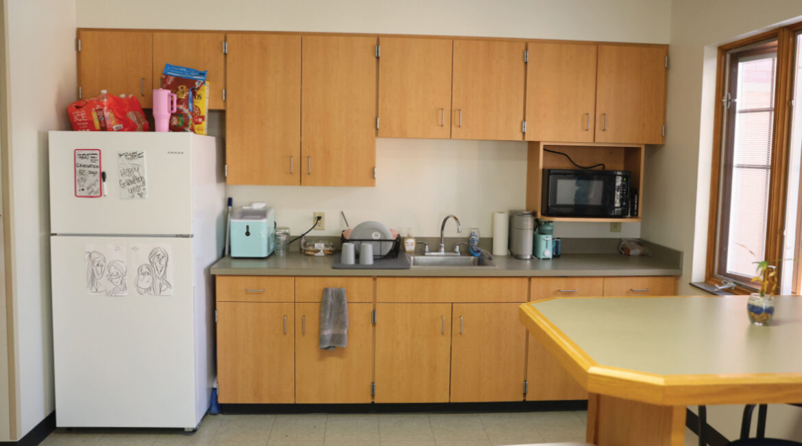 Lags kitchenette showing cupboards, a white refrigerator, kitchen sink, microwave, and a counter high table.