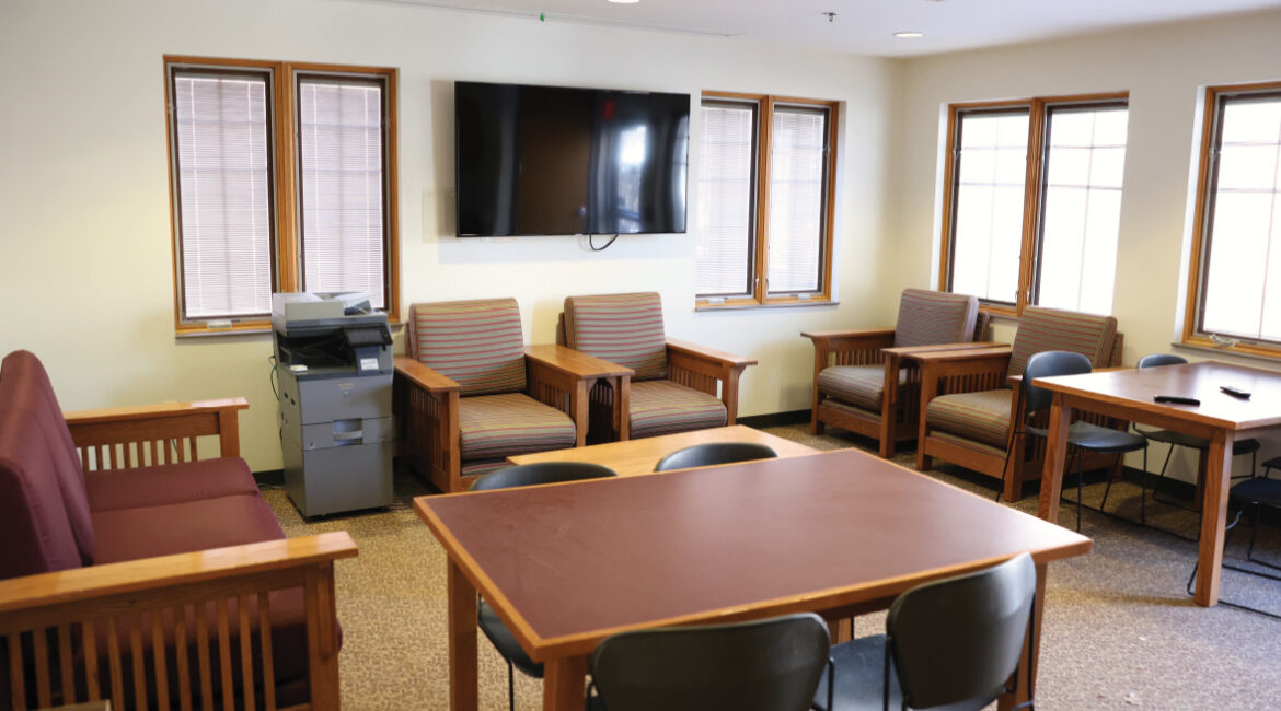 Lags lounge showing comfy chairs, a couch, and two tables with four chairs. A TV is on the wall and a printer is off to the side.
