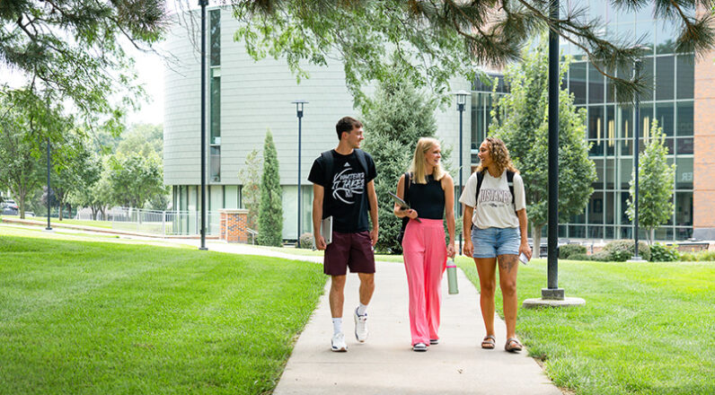 One male and two female students walking on sidewalk talking