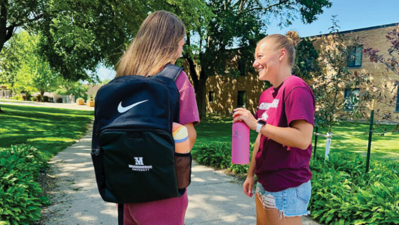 Two students stand talking. One is wearing a Nike backpack and the other is holding an Owala water bottle.