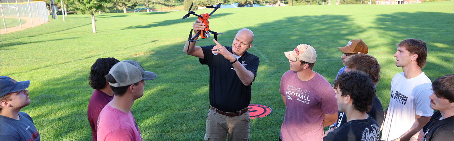 Students gathered around a drone instructor in an outdoor demonstration