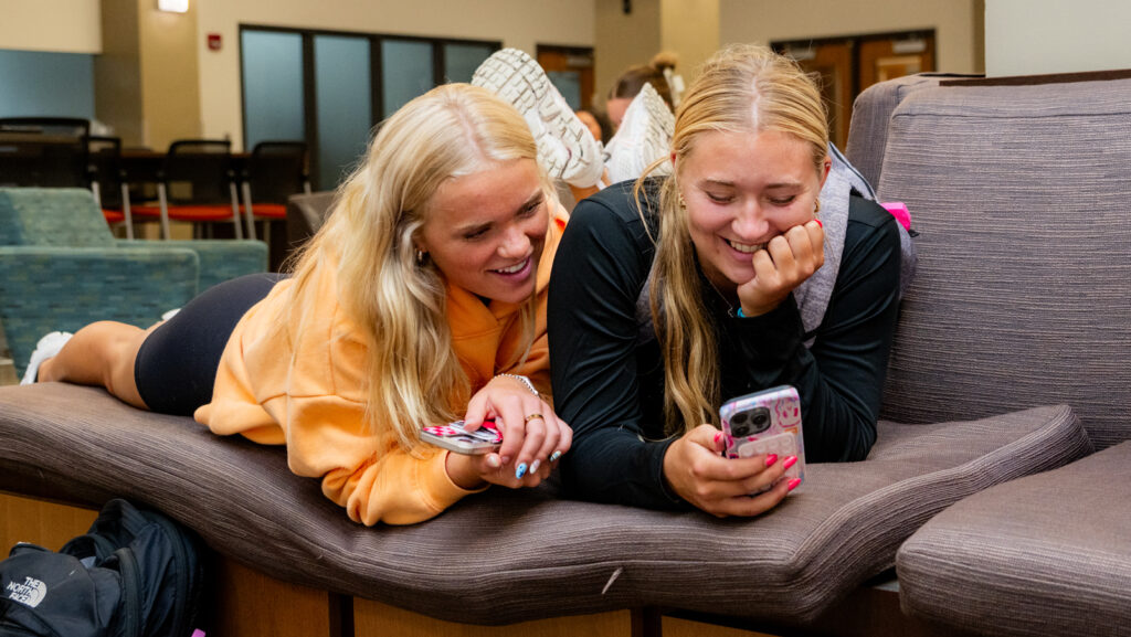 Two students looking at a phone in the residence hall lounge area