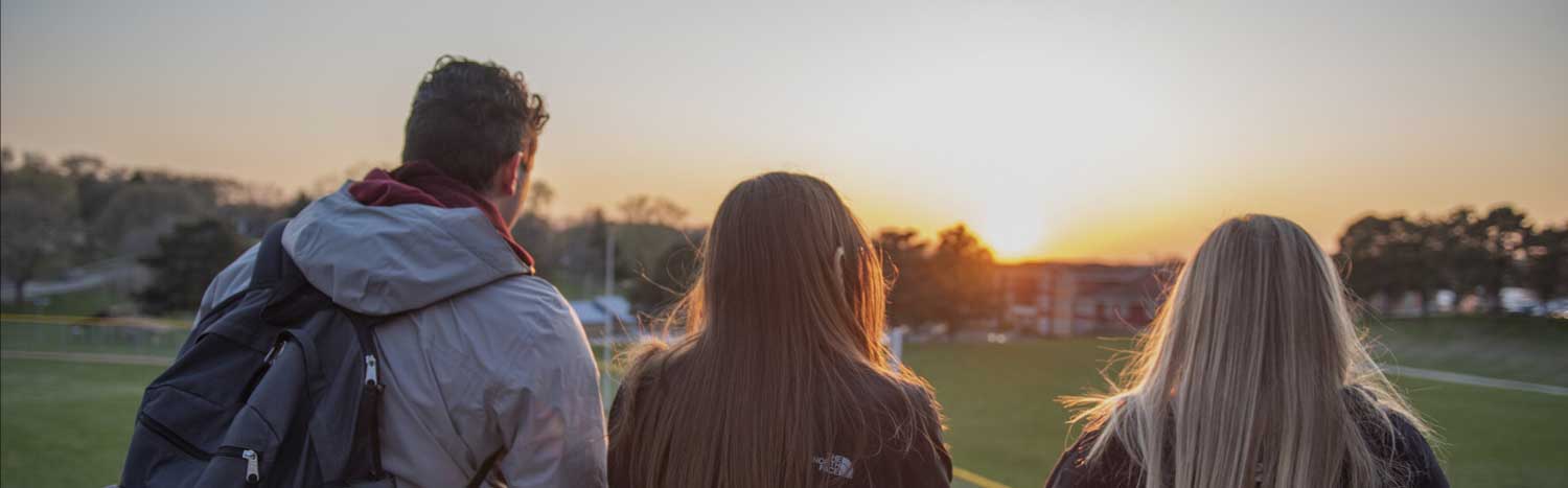 Three Students Looking Over Campus At Sunset