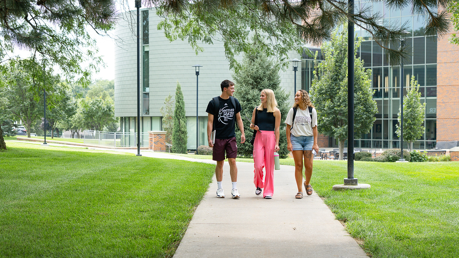 Three Students Walking On Campus By Library