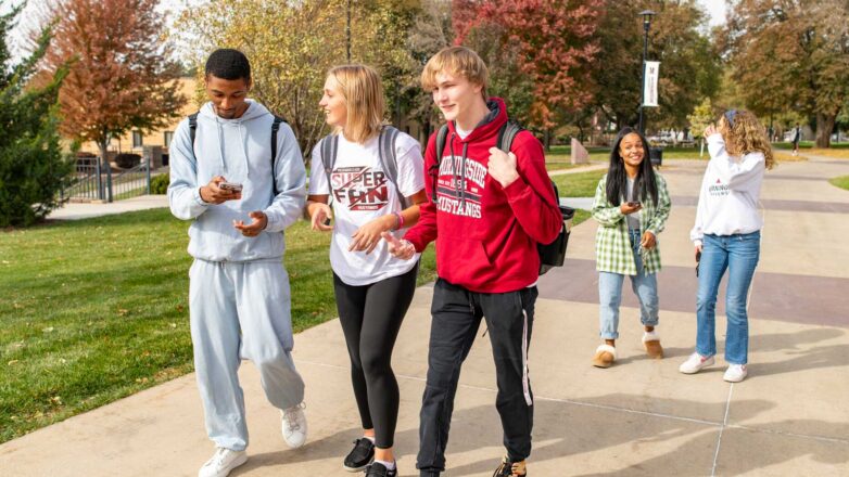 Three Students Walking On Campus With Two Students In The Background