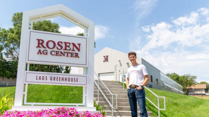 Morningside Ag student stands in front of the Rosen Ag Center and Lags Greenhouse