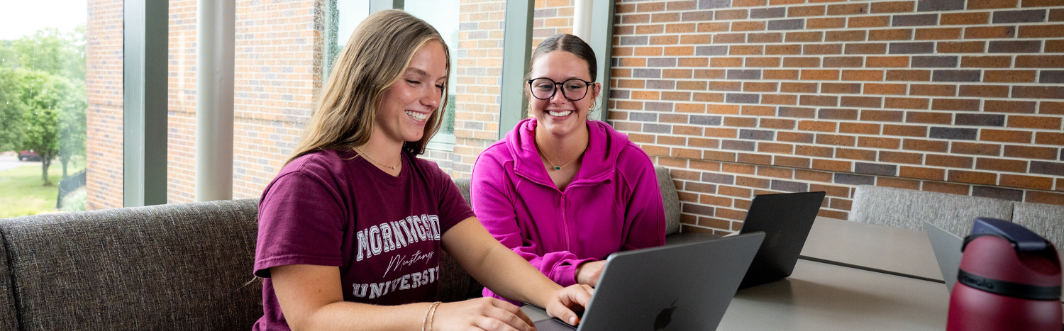 Two students sitting at a table and working on a laptop together
