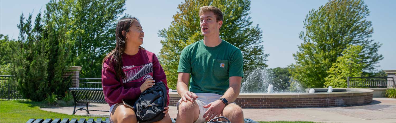 Two Students Sitting On Bench Talking