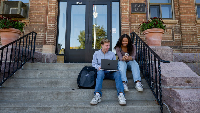Two students sitting on steps in front of Lewis Hall