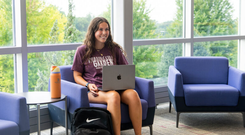 Undergraduate female student sitting with laptop in blue chair
