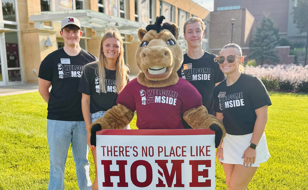 four students stand around Monte the Mustang and a welcome sign