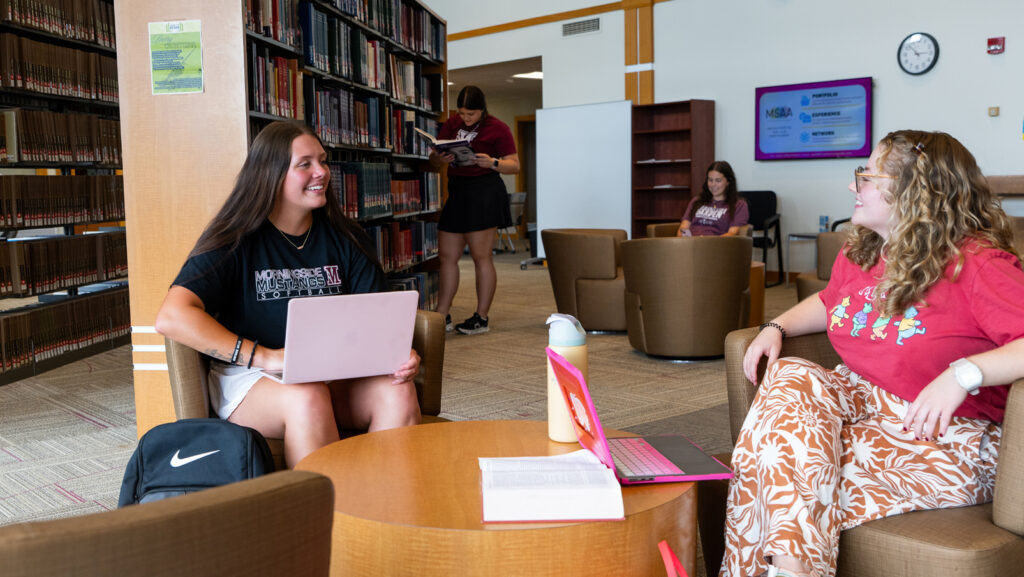 Students gathered around a table in the library and working on their laptops