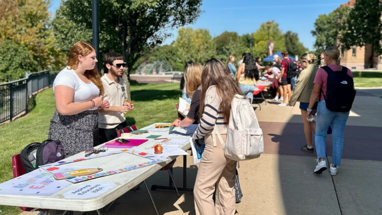 student sitting at a table at the activities fair with two students approaching to talk