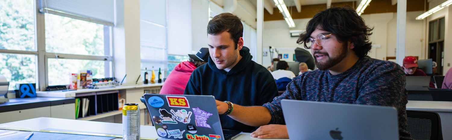 Two students working on their laptops in a classroom
