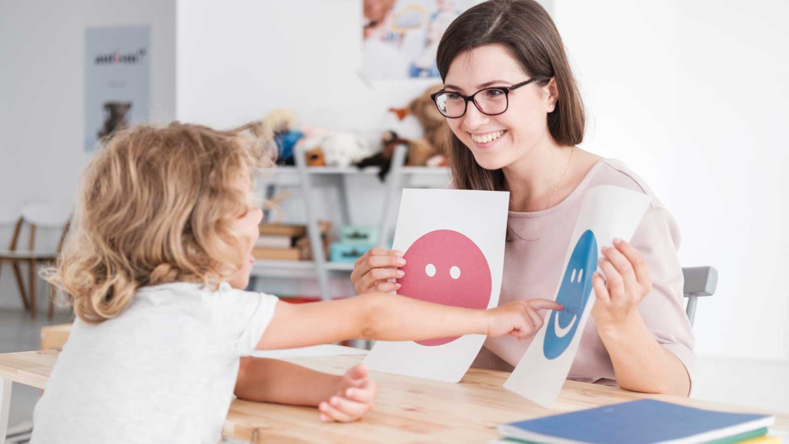 teacher holding up smiley face and sad face to young student