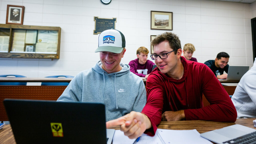 Two students in a classroom working on their computers