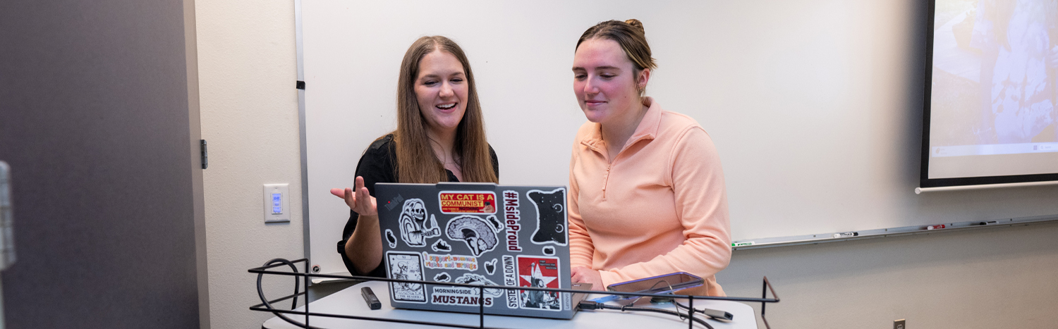 Student and teacher standing in front of a laptop in a classroom