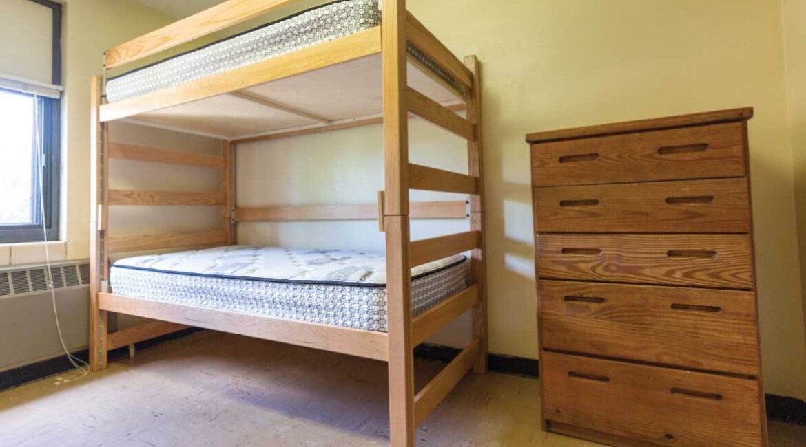 An empty room in Roadman Hall. A bunk bed with a dresser next to it. 