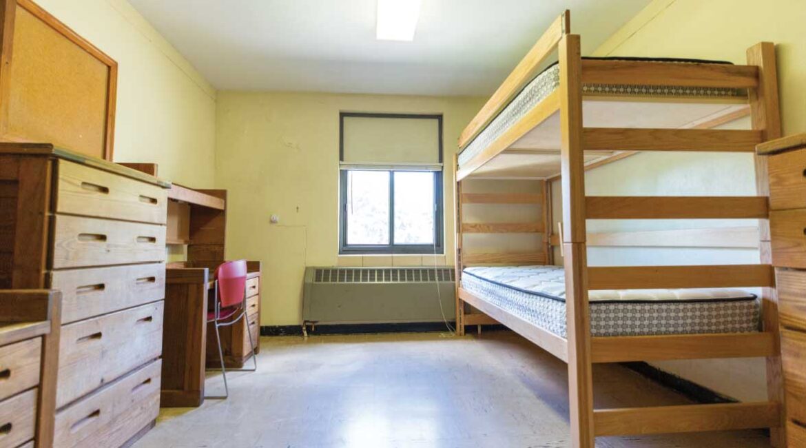 An empty room in Roadman Hall. Two desks and a dresser on the left. A bunk bed and dresser on the right.