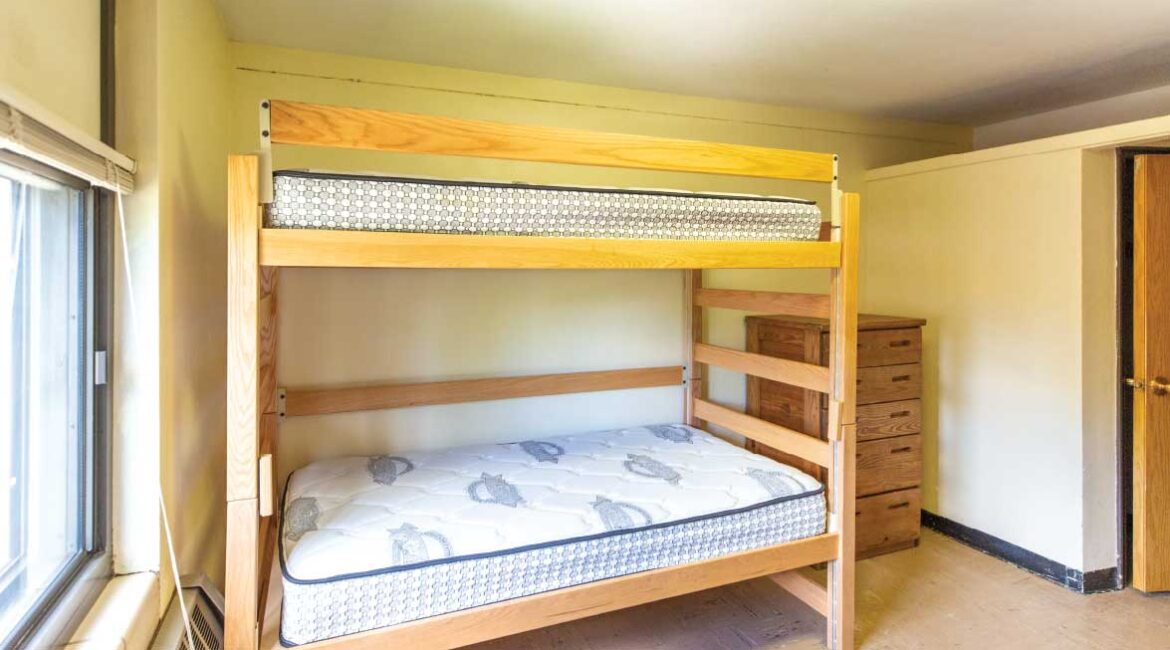 An empty room in Roadman Hall. A bunk bed with a dresser next to it. The door is off to the right. 