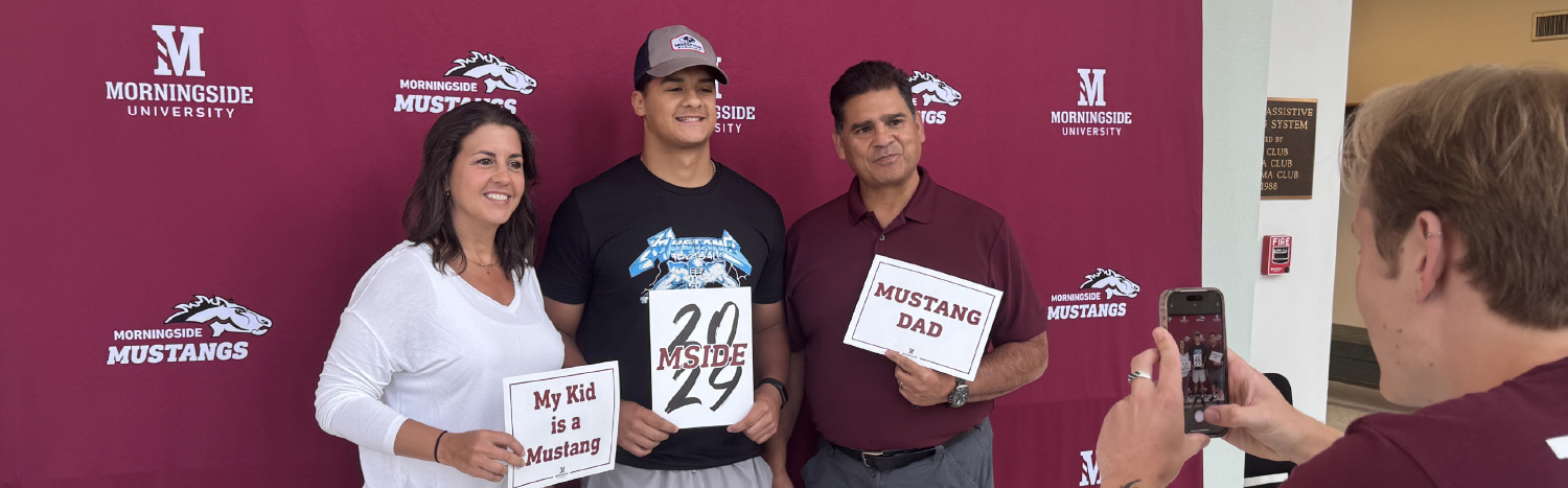student holding a class of 2029 next to his mom and dad while someone takes their photo