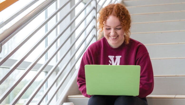 girl sitting on steps smiling at computer