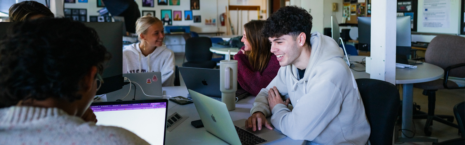 A group of students sitting at a desk using laptops