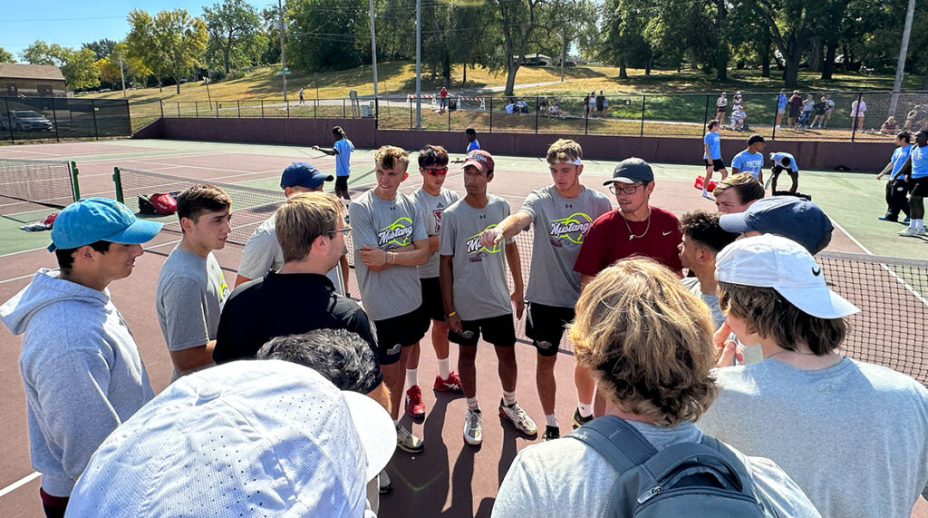 The men's tennis team huddles on the Mason Family Tennis Courts.