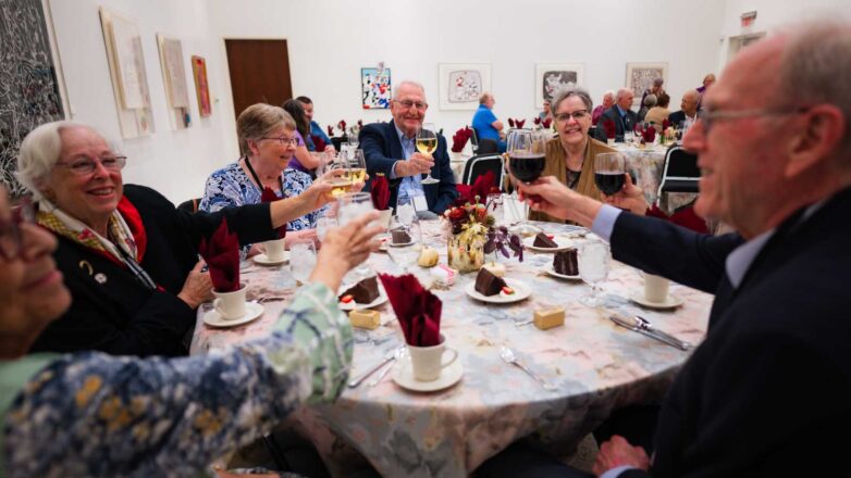 Group of 6 alumni holding up wine glasses at a table.