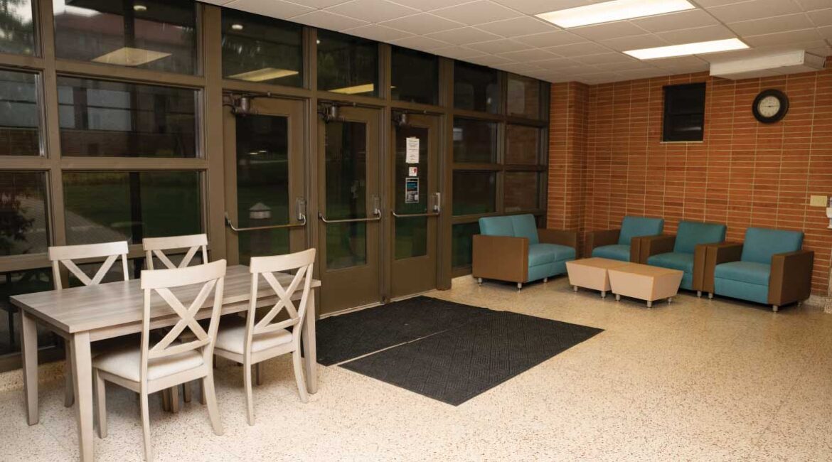 One of the entry ways in Roadman Hall. A table with 4 chairs sits to the left of the doorway. 4 comfortable chairs and a coffee table sit to the right of the doors. 