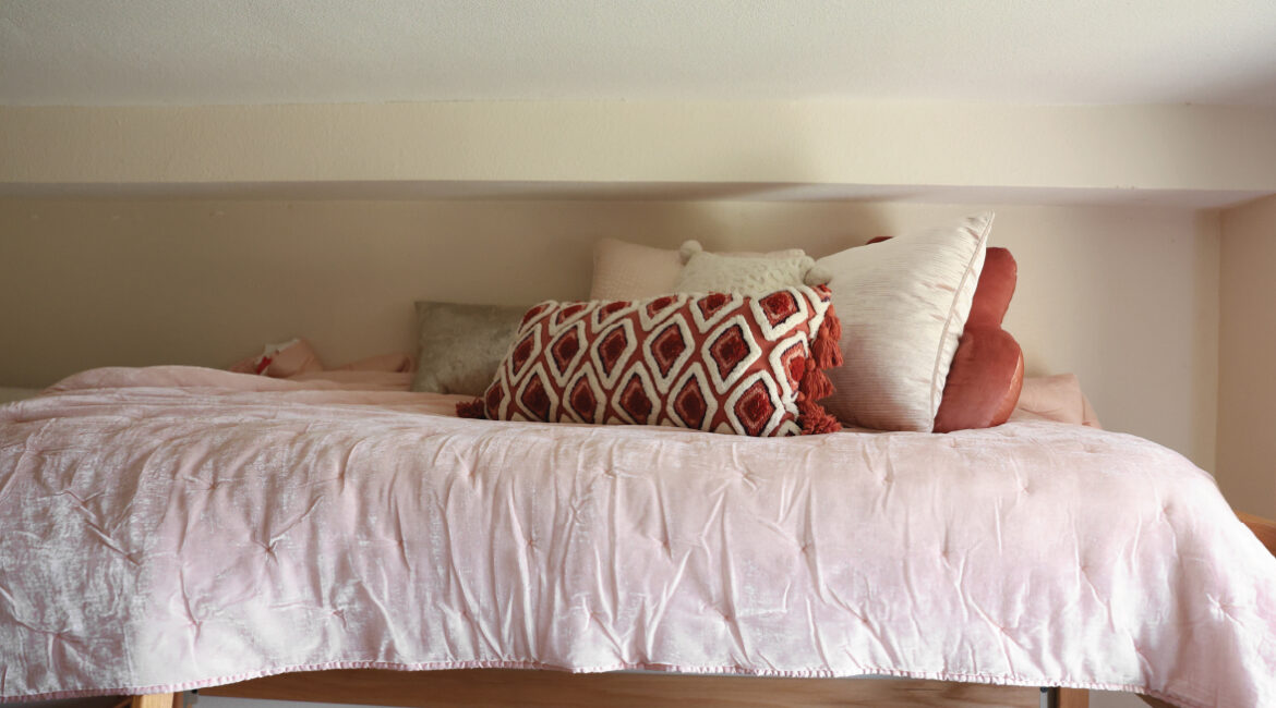 A close up of a lofted bed in Roadman Hall with a pink comforter and pillows on it. 