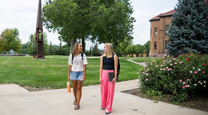 two female students walking with backpacks on campus