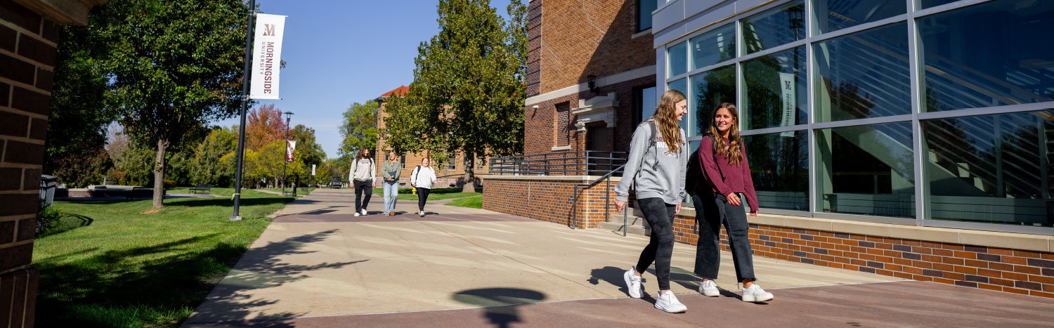 two female students walking on campus outside in front of the learning center.